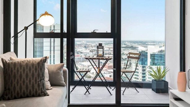 A modern living room with a large window, a sofa, a table, and chairs. - Sierra - Resort Living * Gym Sauna Pool WiFi (Southbank)