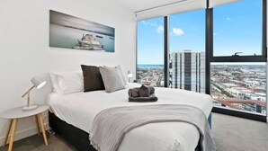 A modern bedroom with a large bed, a bedside lamp, a pillow, a blanket, and a city view through large windows. - Sierra - Resort Living * Gym Sauna Pool WiFi (Southbank)