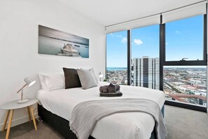 A modern bedroom with a large bed, a bedside lamp, a pillow, a blanket, and a city view through large windows.