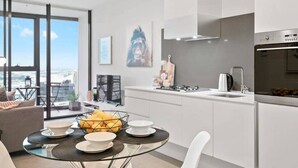 A modern kitchen with a large window, a dining area with a glass table, and a view of the city. - Sierra - Resort Living * Gym Sauna Pool WiFi (Southbank)