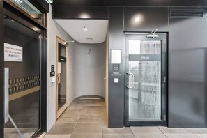 A modern hotel entrance with a glass door labeled 'STEAM,' a sign indicating 'MAX TEMP 44°C,' and a 'Doors Must Be Kept Closed at All Times' sign.