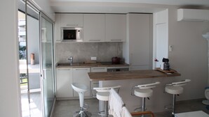 Een moderne keuken met een houten aanrecht, witte barkrukken en een glazen deur naar een balkon.