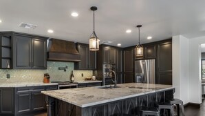 Una cocina moderna con armarios oscuros, una isla grande, electrodomésticos de acero inoxidable e iluminación colgante.