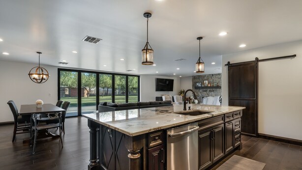Una cocina moderna con una isla grande, armarios de madera oscura e iluminación colgante.
