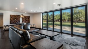 Amplia sala de estar con un sofá grande de cuero negro, una mesa de comedor y vistas a un jardín trasero bien cuidado a través de ventanales de piso a techo.