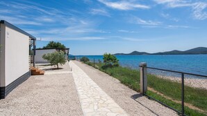 A pathway leading to a building by a lake with boats in the distance. - Mobile Home Plumeria 2 (Biograd)
