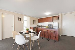 A compact kitchen with a central island, bar stools, and a dining table with chairs.