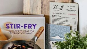 Keittokirja, jonka nimi on ”STIR-FRY – 150 INNOSTAVAA IDEAA ARKIPÄIVÄN RUOANLAITTOON”, sekä ruokalista, jossa on vaihtoehtoina ”BANFF – noutoruokia” ja ”kotitekoista pizzaa”.