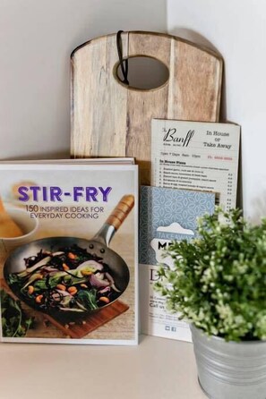 Un livre de recettes intitulé « STIR-FRY, 150 IDÉES INSPIRANTES POUR CUIRE AU QUOTIDIEN » et un tableau de menu proposant les options « BANFF, plats à emporter » et « Pizzas à consommer sur place ».