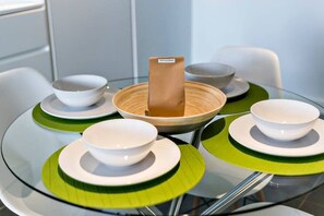 Een glazen tafel met witte kommen en groene placemats, een houten blok met 'WELCOME' erop en een witte stoel.