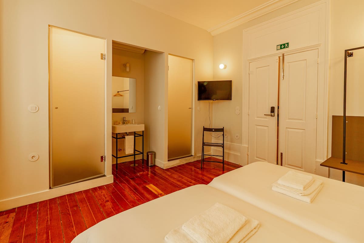 Una habitación de hotel con cama, televisión montada en la pared, baño con espejo y piso de madera.