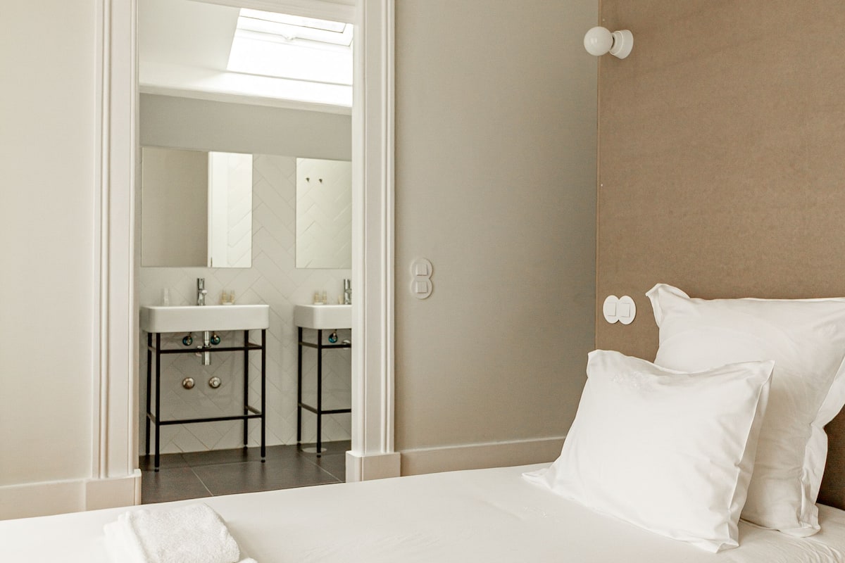 Habitación de hotel con una cama grande, dos almohadas, cabecero, baño con espejo y lavabo.