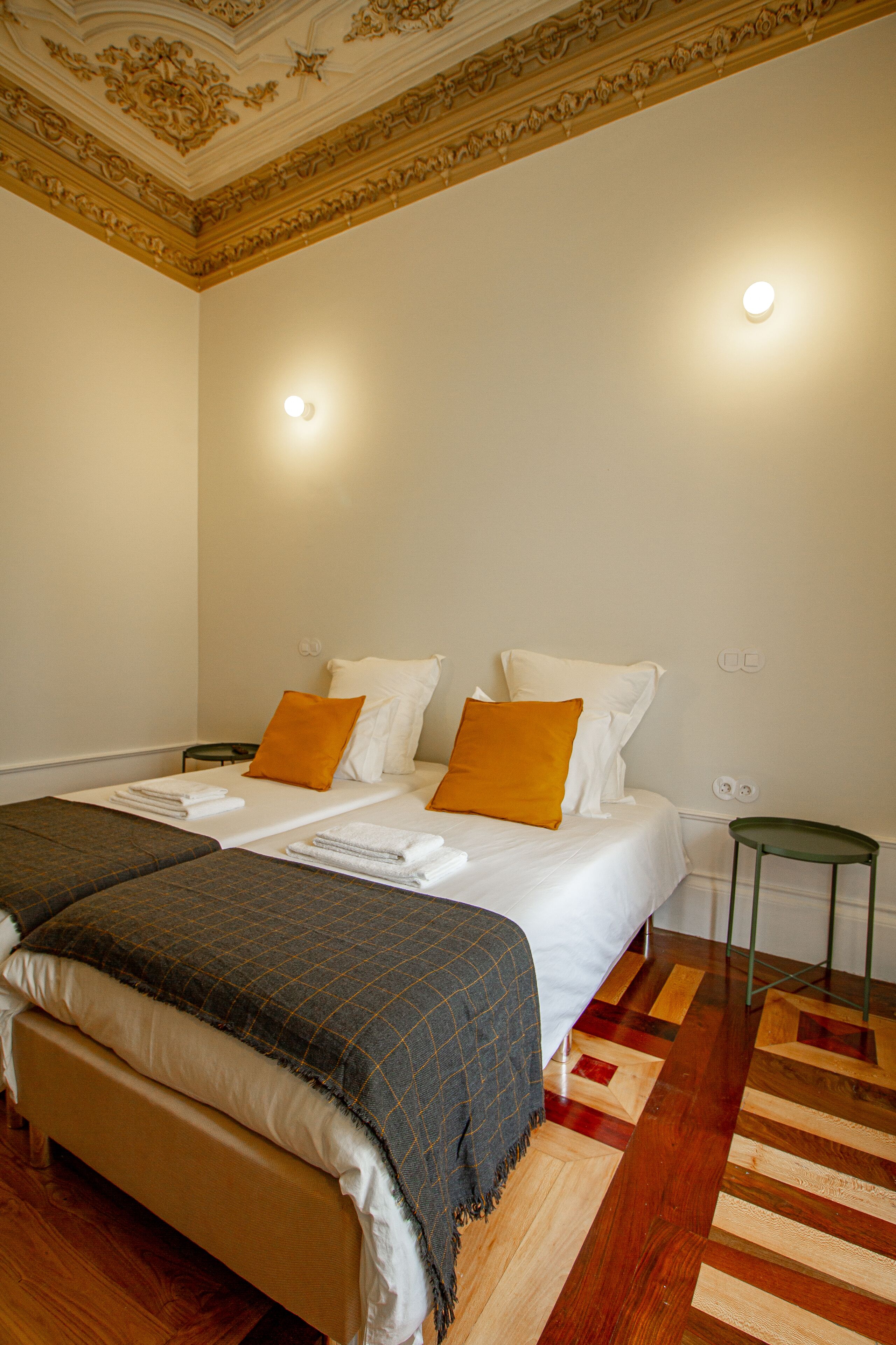 Une chambre d’hôtel avec un grand lit, deux oreillers, une table de chevet verte et un tapis à motifs.