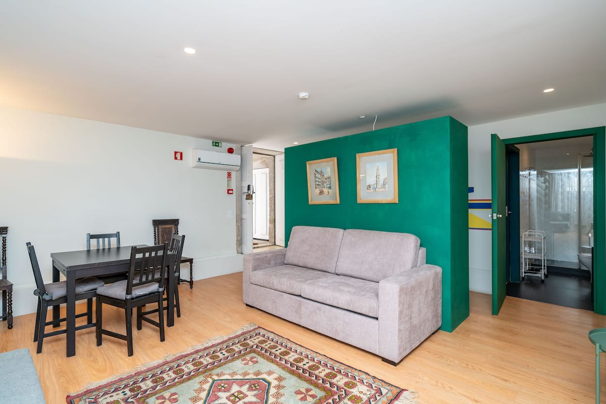 Una habitación con una mesa de comedor, sillas, un sofá, un tapete estampado y una pared verde decorativa.