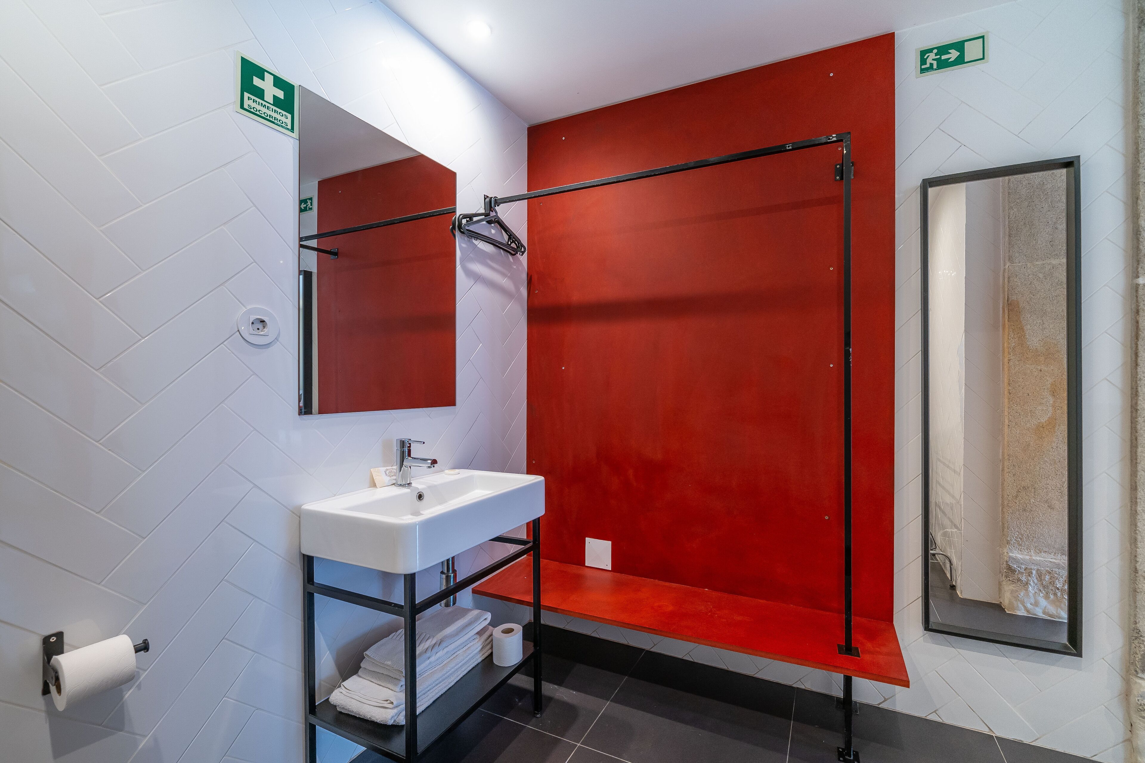 Un baño moderno con un lavabo blanco, un espejo, una cabina de ducha roja y un perchero para toallas.