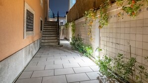Un estrecho callejón con suelo de baldosas, una escalera y una pared adornada con plantas y flores trepadoras.