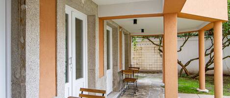 A covered outdoor area with two wooden tables and chairs, a stone pathway, and a grassy area.