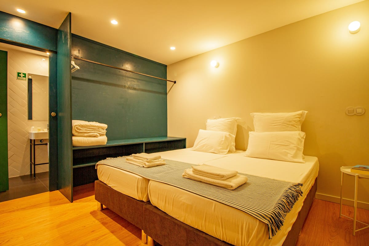 Una habitación de hotel moderna con una cama grande, un banco con toallas, una mesita y una pared verde.