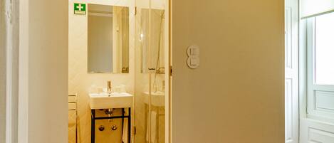 A hotel room with a wooden parquet floor, a white wall, a mirror, a sink, and a door leading to another room.