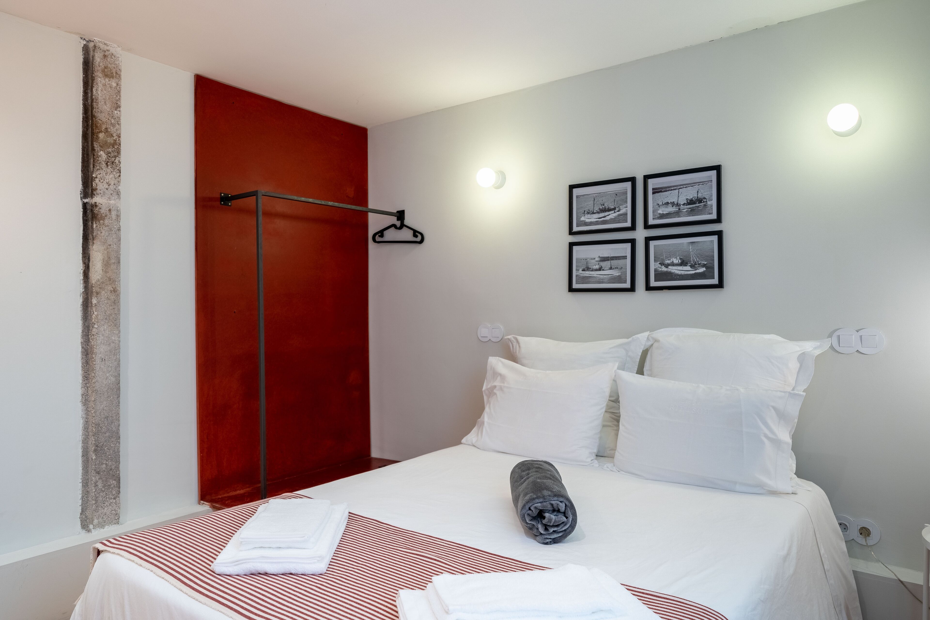 Ein Hotelzimmer mit Bett, weißen Kissen, einer roten Akzentwand, einem Handtuch auf dem Bett und einer Wandleuchte.