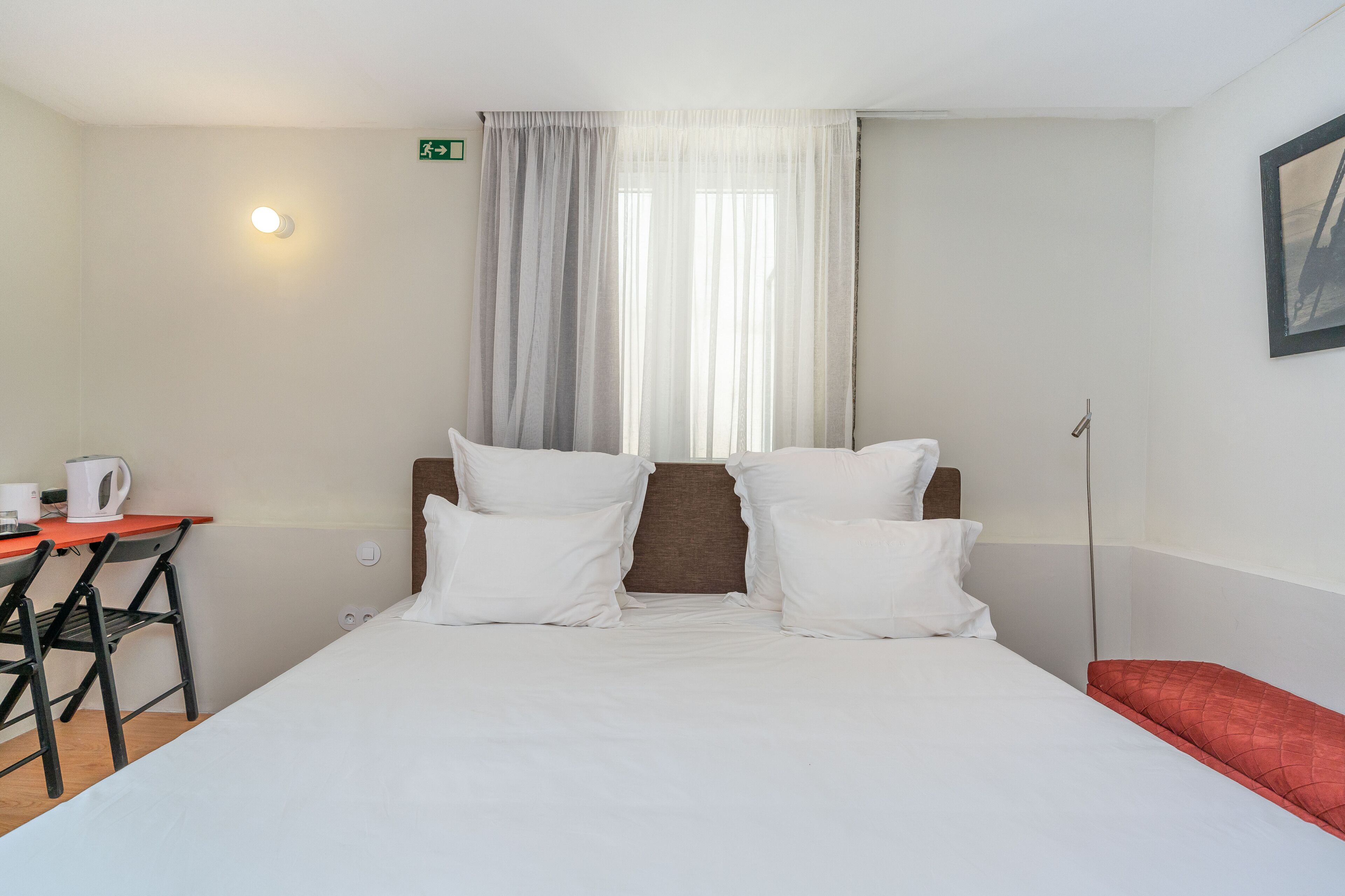 Een hotelkamer met een bed, een bureau met waterkoker en een stoel.