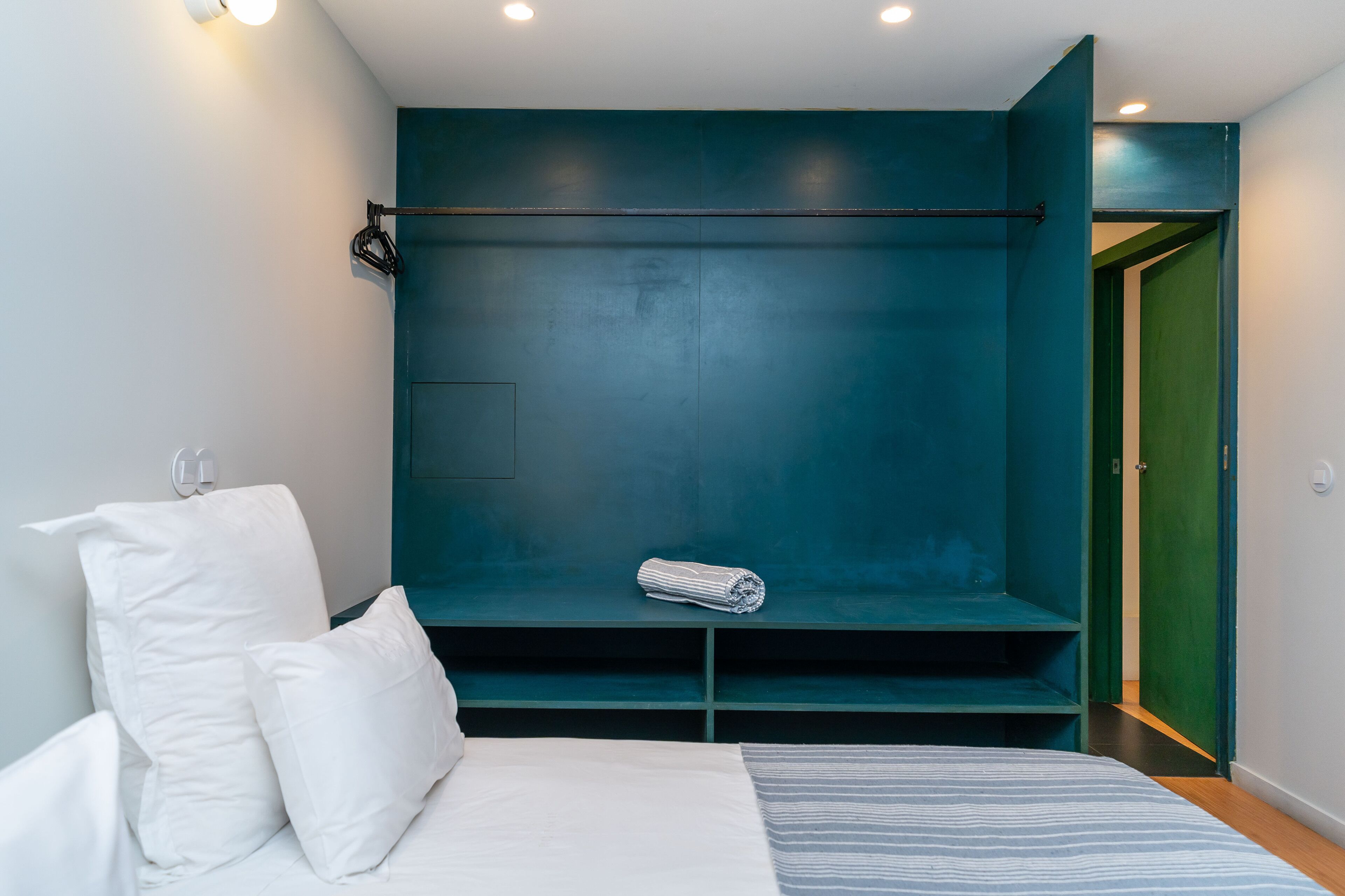 A modern bedroom with a bed, white pillows, a striped blanket, a teal accent wall, and a green door.