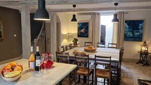 Un coin repas avec une table en marbre, des chaises en bois et des lampes suspendues. On peut voir un panier de fruits et des bouteilles de vin sur la table.