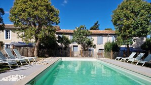 Une piscine avec des chaises longues, une table en bois sur laquelle se trouvent un chapeau, un livre, un pichet vert et des verres.