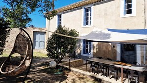 Une terrasse avec une table et des chaises, un fauteuil en osier et un auvent blanc.