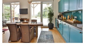 Une cuisine moderne aux armoires de couleur turquoise, un coin repas avec des chaises en osier et une grande plante en pot.