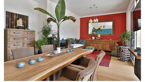 Un salon moderne avec une table à manger en bois, des chaises en osier, un mur d’accent rouge et un grand miroir.