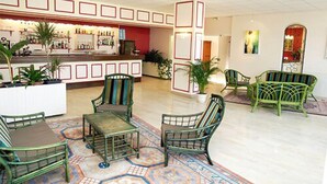 A lobby with a bar area, green chairs, and a patterned rug. - Le Chagny Hotel (Chagny)