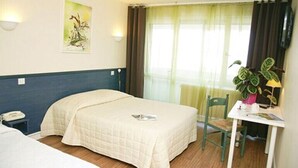 A hotel room with two beds, a small table with a chair, a plant, and a painting on the wall. - Le Chagny Hotel (Chagny)