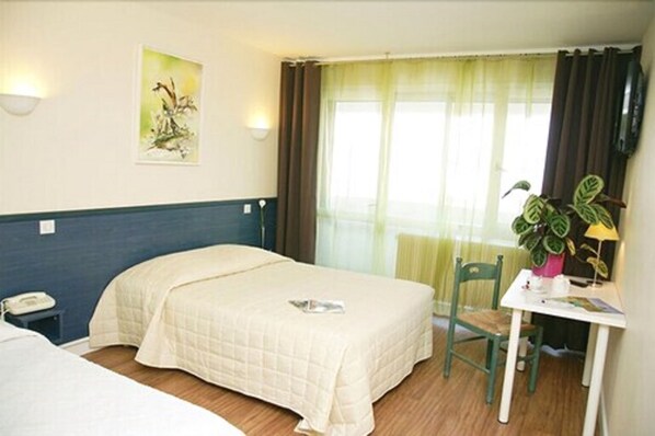 Habitación de hotel con dos camas, una mesita con una silla, una planta y un cuadro en la pared.