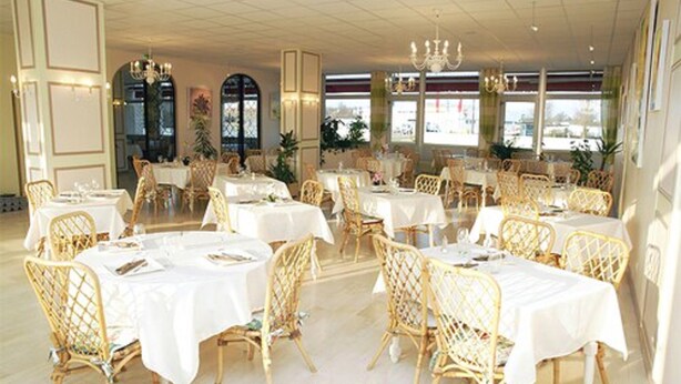 A restaurant with round tables and wicker chairs, large windows, and chandeliers. - Le Chagny Hotel (Chagny)