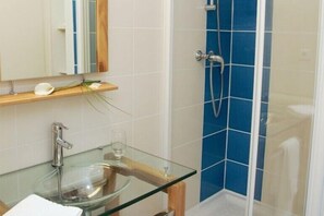 A bathroom with a glass sink, a mirror, a shower with blue tiles, and a wooden shelf with a white flower and green leaves. - Le Chagny Hotel (Chagny)