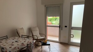 Uma sala de jantar com uma mesa coberta por uma toalha florida, duas cadeiras e uma mesinha com uma cesta.