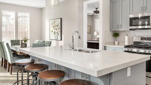 A modern kitchen with a large island, bar stools, and a dining area with chairs. - Desert Escape at Ladera (Washington)