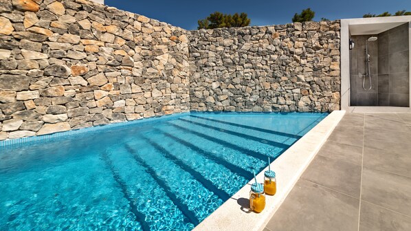 Piscina com paredes de pedra e área de chuveiro.