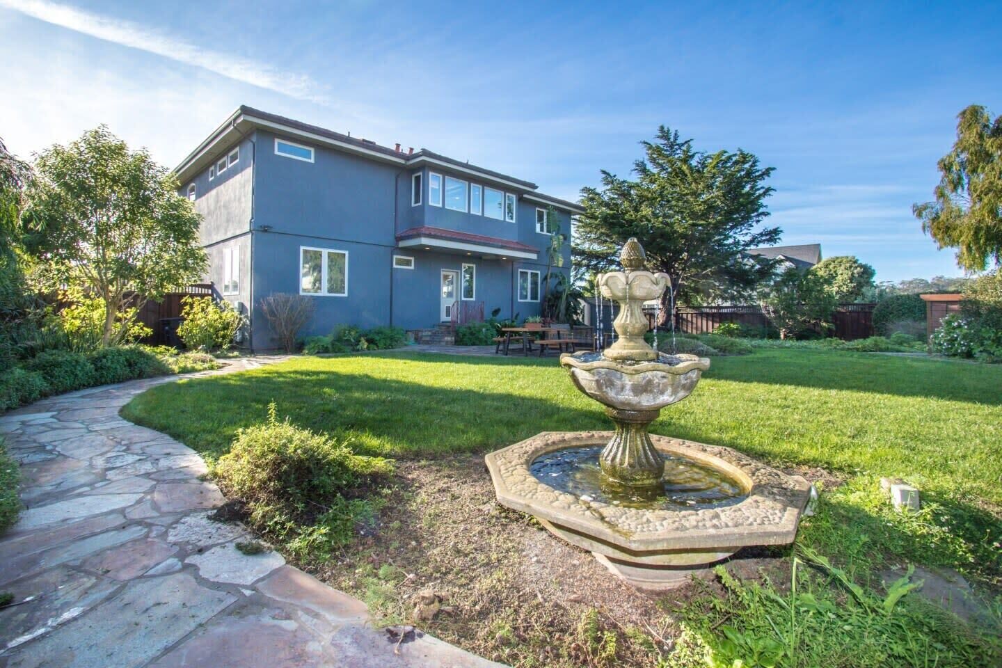 A house with a stone pathway leading to a fountain in the yard.