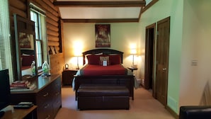 Un dormitorio con una cama con cabecera de madera, dos lámparas de noche, una mesita de noche, un aparador y un espejo.