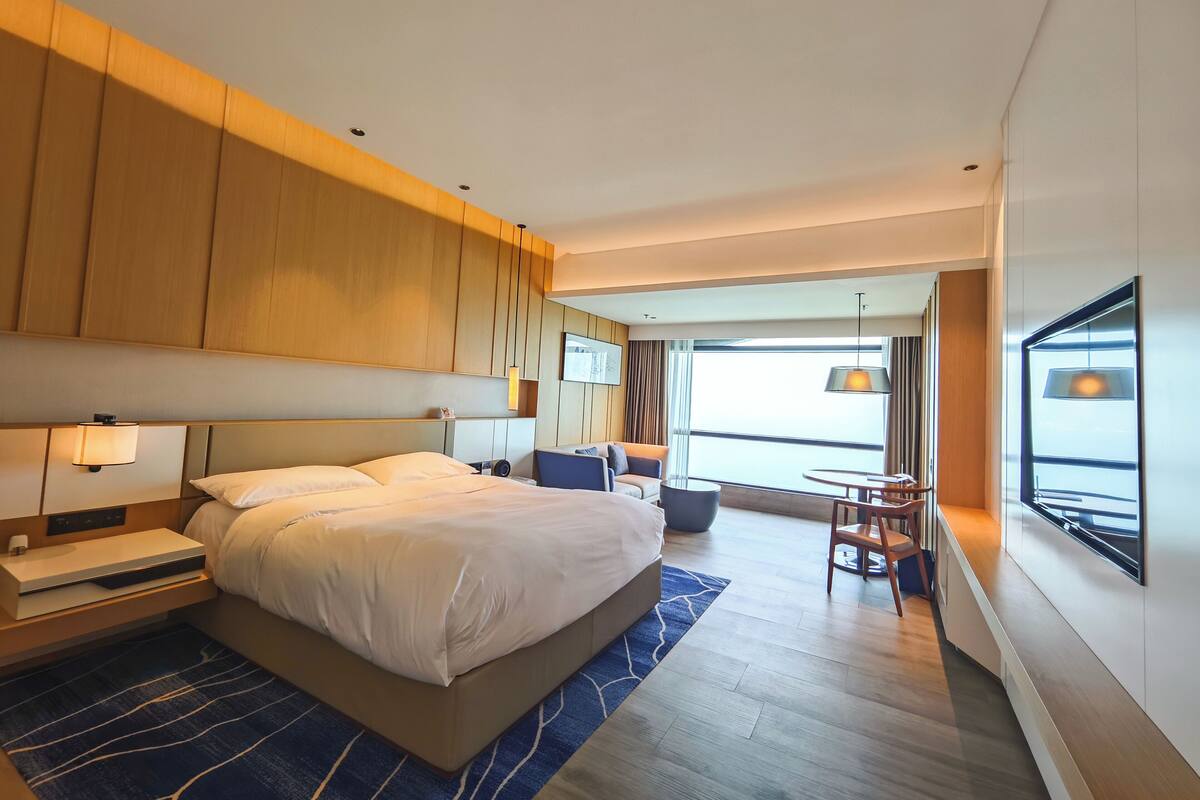Een moderne hotelkamer met een groot bed, een bureau, een stoel en uitzicht op de stad door het raam.