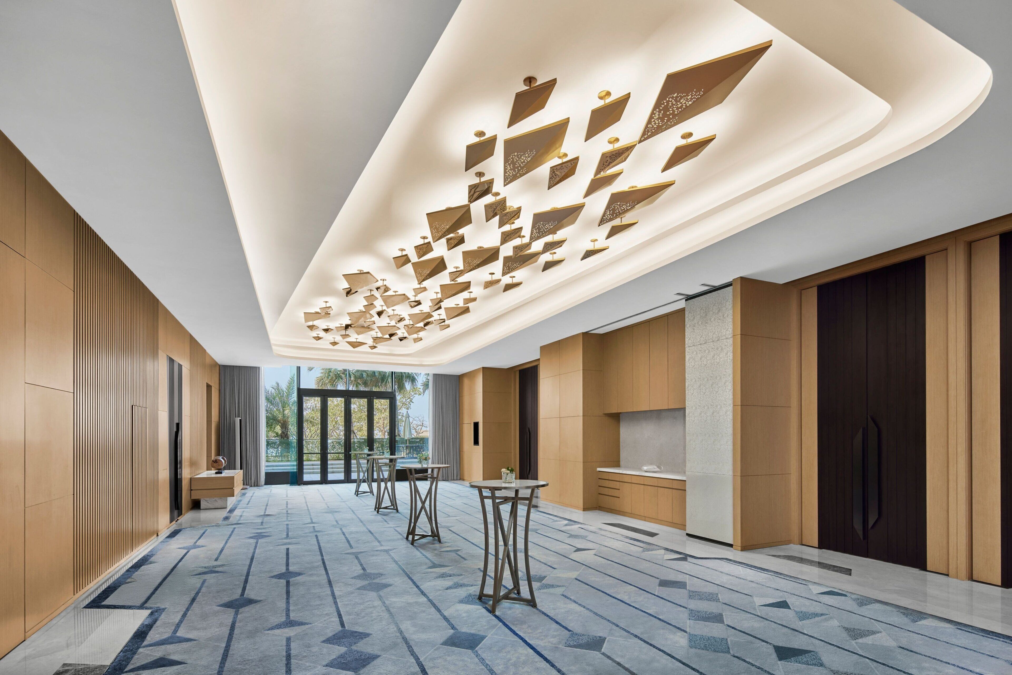Um hall de hotel moderno com piso de padrão geométrico, painéis de madeira e teto com designs geométricos iluminados.