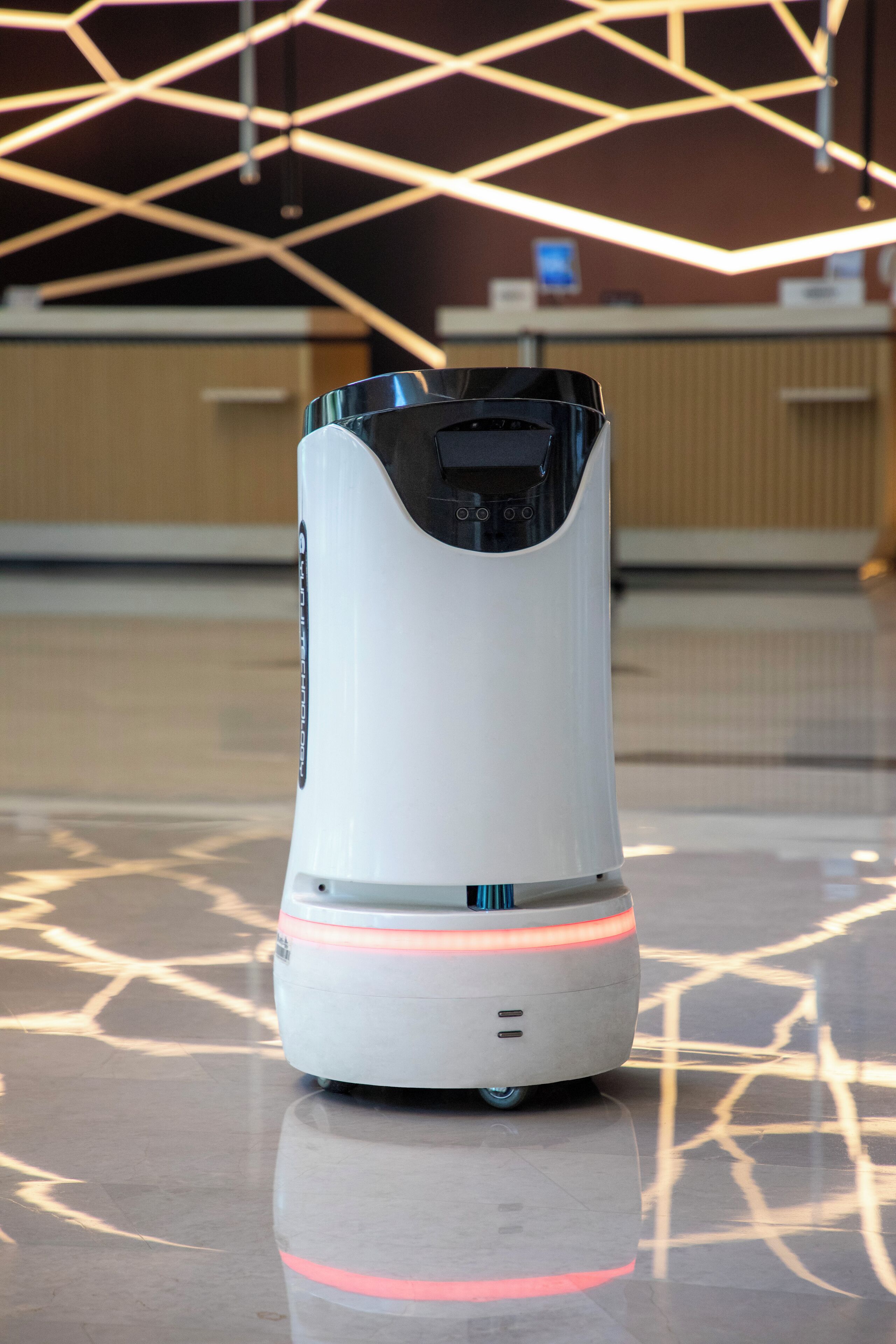 Un robot in un'elegante hall con luci a soffitto geometriche e pavimento lucido.