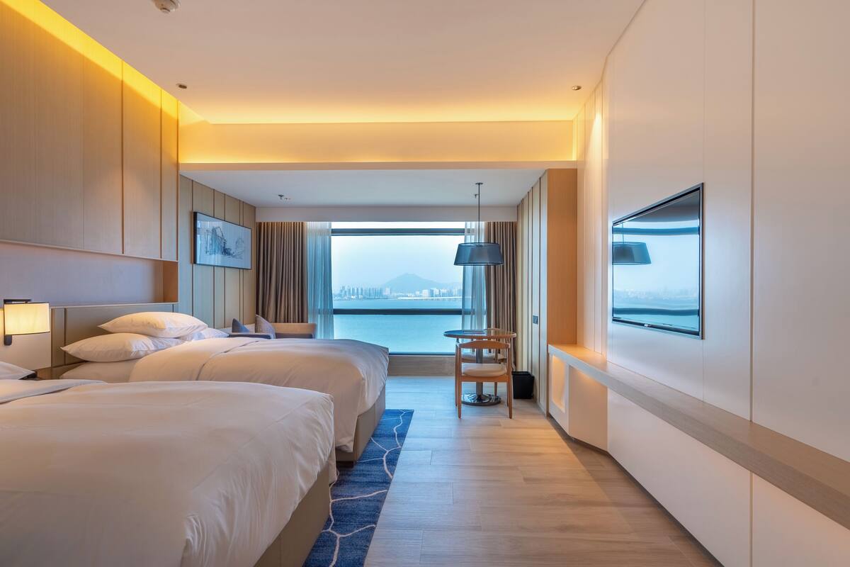 Hotelkamer met twee bedden, een groot raam en uitzicht op de stad, een bureau en een stoel.