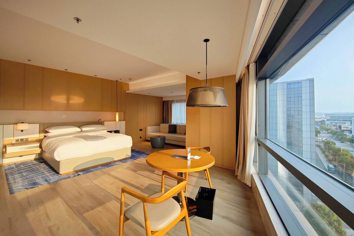 Een moderne hotelkamer met een groot bed, een bank, een eettafel en uitzicht over de stad.