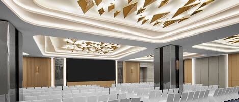 Une salle de conférence moderne, avec des rangées de chaises blanches, un grand écran et un plafond orné de motifs.