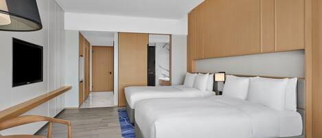 A hotel room with two beds, a TV mounted on the wall, a wooden desk, and a blue patterned rug.