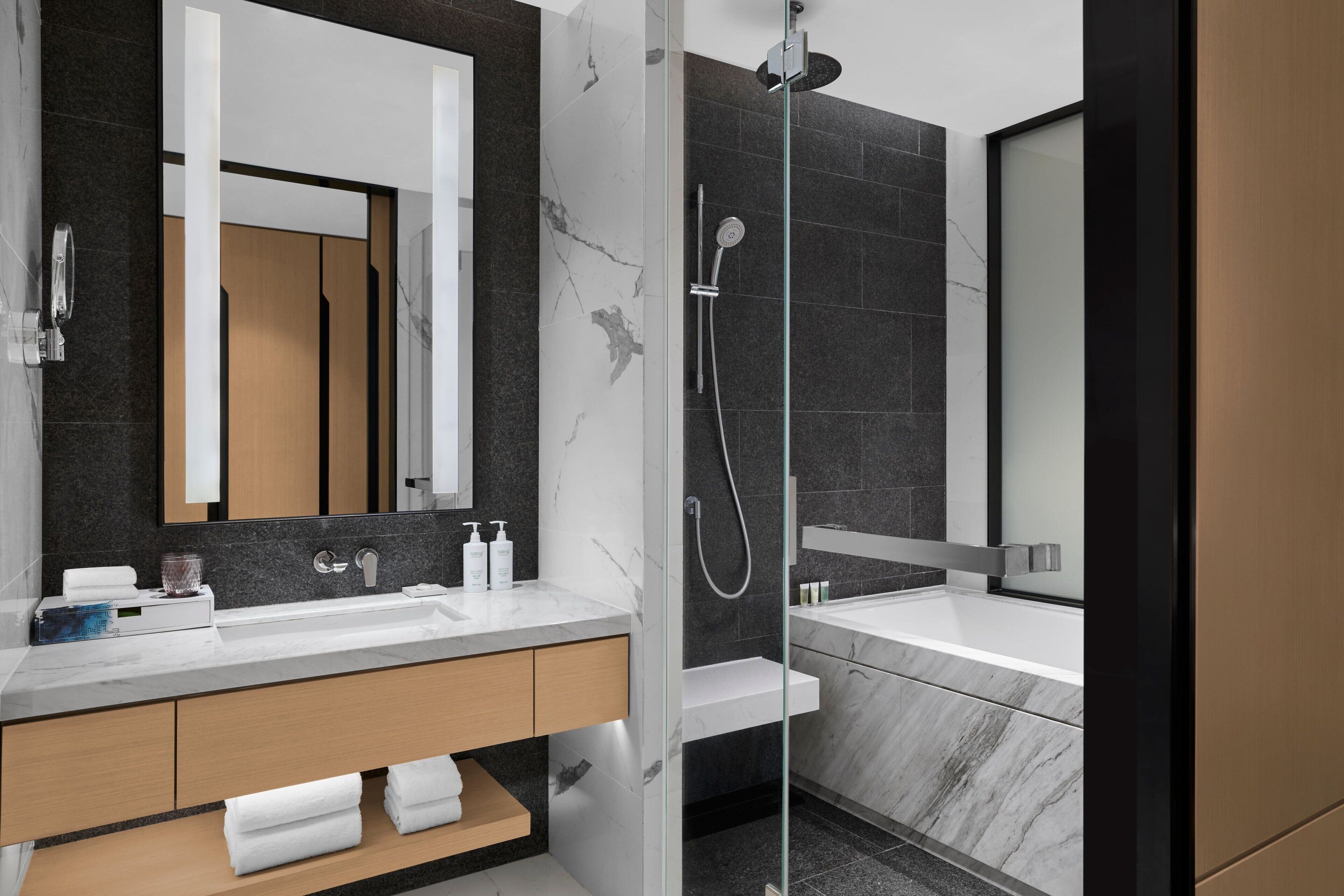 A modern bathroom with a glass-enclosed shower, a large mirror, and a vanity with a marble countertop.