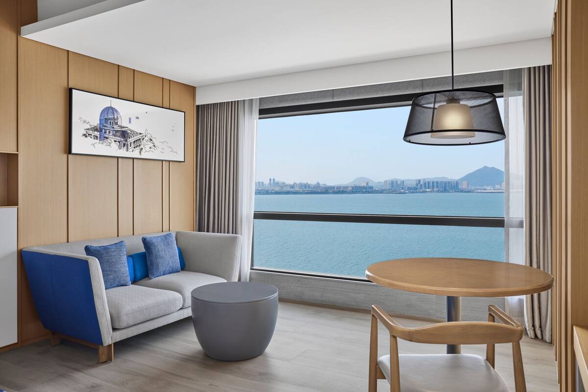 Een moderne woonkamer met een bank, een ronde tafel en uitzicht op een stadsbeeld en water.